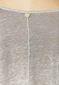 Vaaleanharmaa neulepaita, jossa on pyöreä pääntie. Takana on pieni pyöreä tunnus, ja paidassa on hienovarainen tekstuuri sekä sauma keskellä.