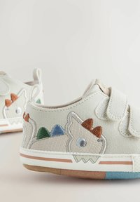 Jasnoszare skórzane buty z haftem dinozaura w zielonym, niebieskim i pomarańczowym kolorze. Posiadają zapięcia na rzepy i teksturowaną podeszwę.