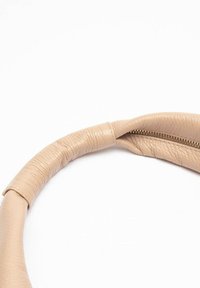 Borsa a tracolla circolare in pelle beige con superficie testurizzata e dettaglio della cerniera dorato. Il manico è avvolto per maggiore comfort e aderenza.