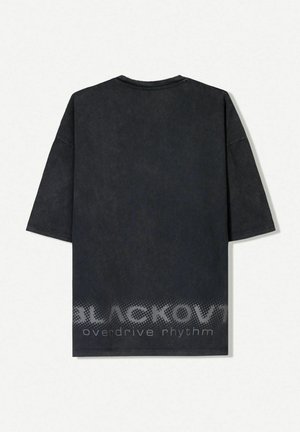 Black oversized t-shirt in dark gray with a rounded neck, short sleeves, and a textured finish. Features printed text at the hem.