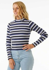 Langärmliges, hochgeschlossenes Oberteil in Schwarz, Weiß und blauen horizontalen Streifen. Gerippte Textur mit körperbetontem Design, kombiniert mit hellblauen Jeans.