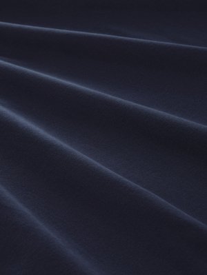 Marineblauer Baumwollstoff mit glatter Textur und sichtbaren Falten, der eine gleichmäßige Farbe mit leichtem Glanz aufweist, der das Licht reflektiert.