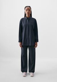 Mørkeblå bluse med krage og lange ærmer, parret med matchende løse bukser og lyserøde sneakers. Enkel design og glat tekstur.