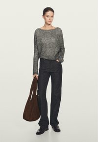 Grå, struktureret sweater med bred udskæring, mørkeblå jeans og en brun suede tote taske. Model der står med hænderne i lommerne.