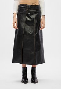 Μαύρη δερμάτινη μίντι φούστα με ορατές ραφές, ζώνη στη μέση κα�ι μπροστά σχισμή. Συνδυάζεται με μαύρες μπότες αστραγάλου.