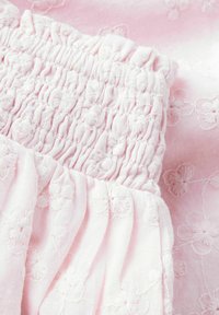 Tessuto rosa chiaro con motivi floreali ricamati e dettagli smock, con una texture morbida e un design drappeggiato.