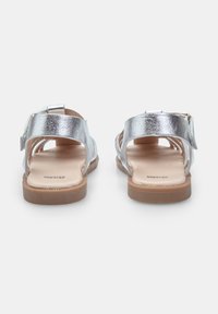 Zilverkleurige metallic sandalen met een verstelbare enkelband, platte zool en open teenontwerp, met een soepele textuur en een minimalistische stijl.