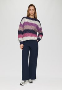 Gebreide trui met brede strepen in paars, roze en marineblauw. Gecombineerd met marineblauwe wijde broek en metallic sneakers.