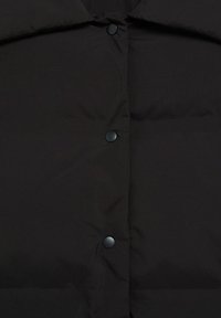 Veste matelassée noire à l'avant avec trois boutons-pression mats alignés verticalement au centre.