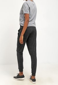 Grå bomullströja och svarta träningsbyxor med texturerad yta, med elastiska mudd, bärs med svarta sneakers.