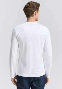 Langærmet hvid T-shirt med rund halsudskæring. Lavet af glat stof, med en tætsiddende silhuet og enkel design, kombineret med blå denimjeans.