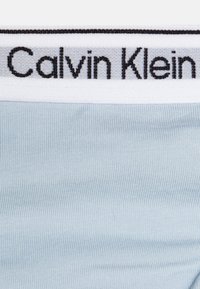 Svetlomodrý bavlnený pás boxeriek s čiernym vyšitým logom "Calvin Klein" na bielom pásiku. Hladká textúra, jednoduchý dizajn a mäkká látka.