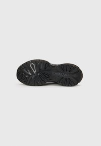 Semelle de chaussure de sport noire avec des motifs de semelle profonde, une finition texturée et des crampons distincts pour l'adhérence et la traction. Présente une semelle intermédiaire noire lisse.