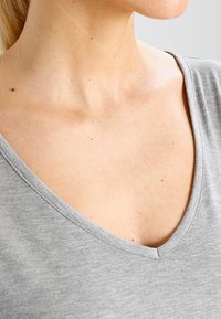 Graues V-Ausschnitt-T-Shirt aus weichem, leichtem Stoff mit einer subtilen melierten Textur. Zeigt den Ausschnitt und den Schulterbereich.
