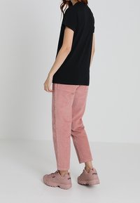 Camiseta negra de manga corta, pantalones de pana rosa y zapatillas de deporte rosa claro con marca. El conjunto es casual y tiene un ajuste relajado.