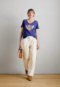 Ναυτικό μπλουζάκι V με γραφικό σχέδιο, κρέμα παντελόνι με φαρδιά πόδια, καφέ μποτάκια μέχρι τον αστράγαλο και μια μικρή καφέ τσάντα χειρός με λευκές λεπτομέρειες.