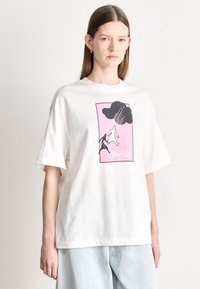 Valge puuvillane T-särk, mis on lõdvalt istuv, kujundusega roosas, mustas ja valges, kujutades pilve all vihma all olevaid figuure.