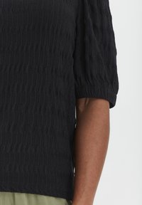 Top nero strutturato con maniche corte, leggermente a sbuffo e una vestibilità comoda, con un motivo ondulato e un tessuto liscio e morbido.