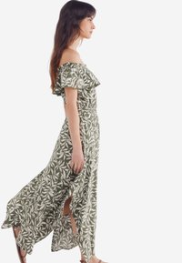 Grünes Off-Shoulder-Kleid mit weißem Blättermuster, Rüschenausschnitt und seitlichen Schlitzen, aus leichtem Stoff gefertigt.
