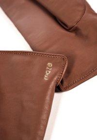 Brune læderhandsker med en glat tekstur og detaljerede syninger, med et diskret gyldent logo i hjørnet.