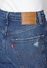 Gros plan sur la poche arrière d'un jean Levi's en denim bleu, avec des détails usés et une étiquette en cuir beige au-dessus de la poche.