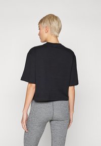 Fekete, rövid ujjú, puha pamutból készült crop felső, kerek nyakkivágással és egyszerű dizájnnal. Szürke leggings-szel kombinálva.
