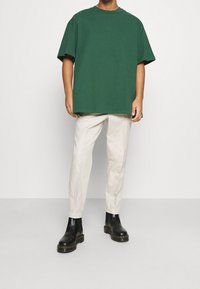 T-shirt vert en coton oversize à manches courtes, associé à un pantalon crème léger à jambes droites et des bottines noires.