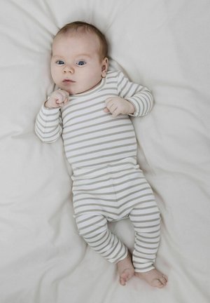 Csíkos bébi rugdalózó fehér és világosszürke színben, amely hosszú ujjú és testre simuló szabású. A baba egy puha, világos színű felületen fekszik.