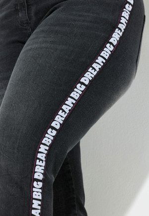Jeans de denim negro con un atrevido texto en blanco y rosa "BIG DREAM" a lo largo de la costura lateral, con un diseño ajustado y tejido texturizado.