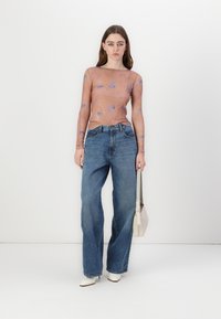 Langermet gjennomsiktig topp i fersken med blå mønstre, sammen med løse blå jeans og hvite spisse ankestøvletter. Bærer en liten lys veske.