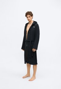 Robe de banho preta com capuz, em tecido de felpa suave, com mangas compridas, cinto de laçar e um pequeno logótipo no peito.