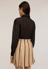 Camicia nera trasparente a maniche lunghe abbinata a una gonna beige con righe verticali nere e una vita elastica.