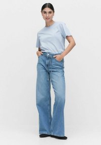 Vaaleansininen lyhythihaisen t-paita, joka on yhdistetty korkeavyötäröisiin, leveälahkeisiin sinisiin farkkuihin. Ominaisuuksiin kuuluu rento istuvuus ja nyöri vyötäröllä.