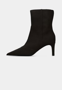 Bota preta ankle feita de camurça, com biqueira pontuda e um salto fino. O design é elegante, com uma textura suave e uma silhueta minimalista.