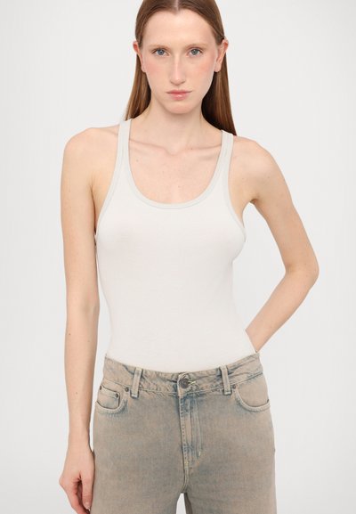 Weißes geripptes Tanktop mit breiten Trägern, kombiniert mit hellblauen Denim-Jeans mit klassischen Taschen und einem Knopfverschluss.