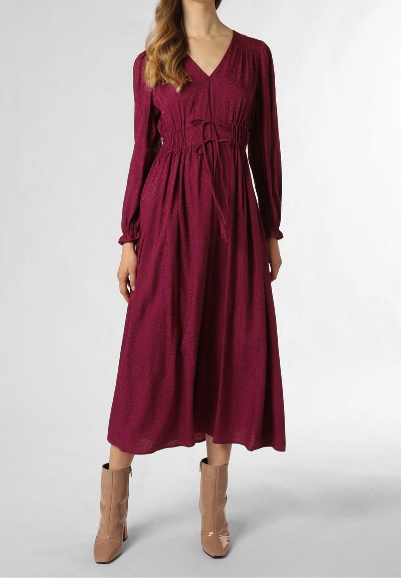 Robe bordeaux à manches longues avec un décolleté en V et une taille élastique, présentant une texture subtile. Associée à des bottines marron clair.