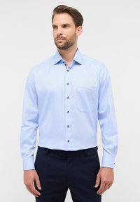 Camicia a maniche lunghe blu chiaro con colletto a punta, bottoni marroni e taschino sul petto, realizzata in un tessuto liscio.
