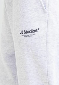 Sivi pamučni dukserica s mekom teksturom, bočnim džepovima i logotipom "JJ Studios" u crnom vezu na prednjem dijelu.