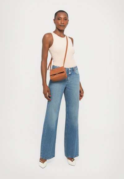 Beige fitted tank top, blue flared jeans, brown crossbody bag, white pointed toe shoes with black accents; smooth fabric, casual style.
