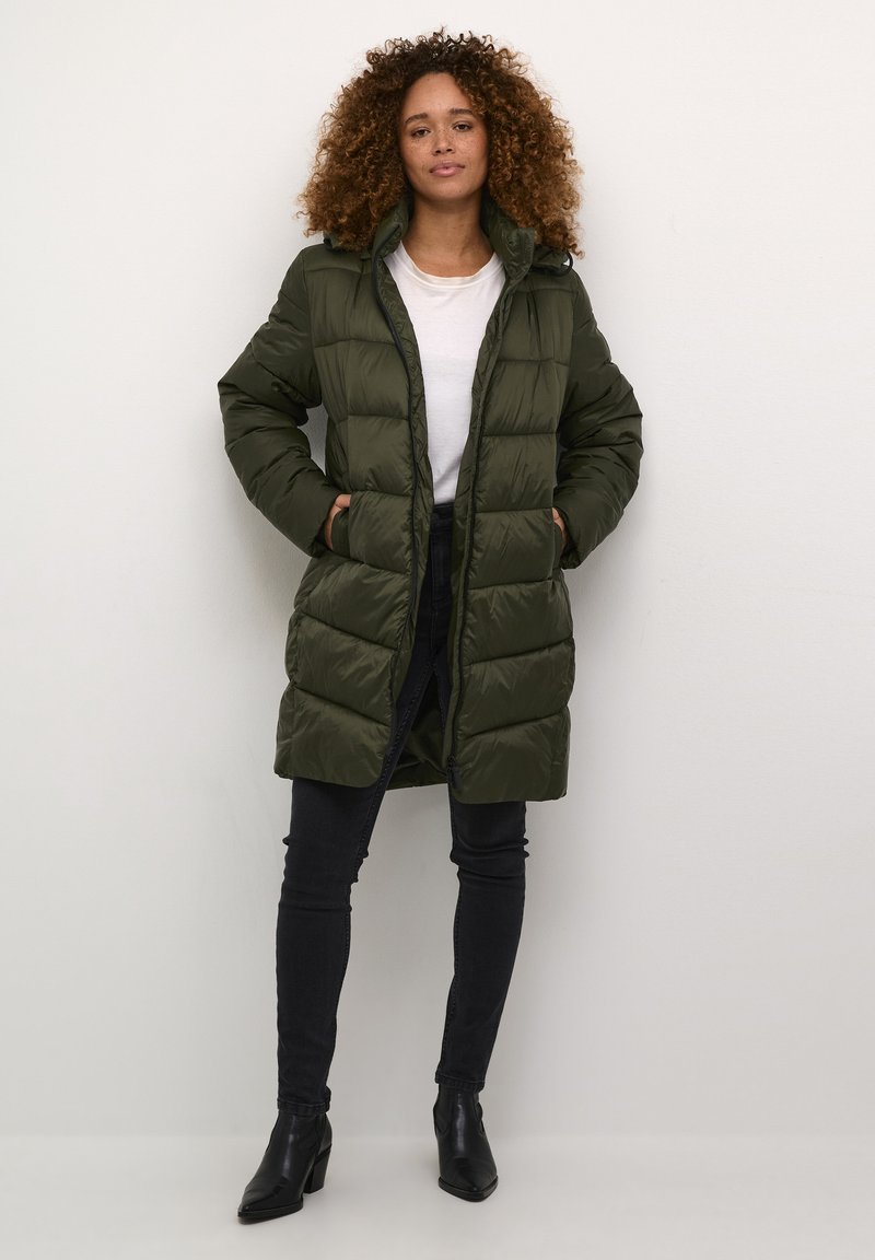 Olijfgroen pufferjack met een gequilt patroon, ritsluiting en zijzakken. In combinatie met strakke zwarte jeans en enkellaarsjes.