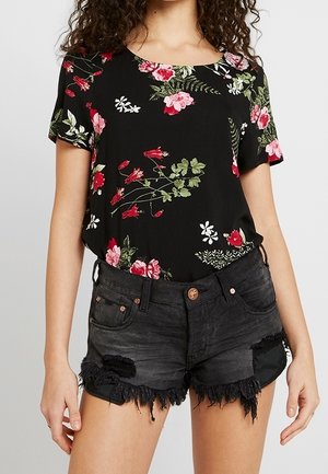 Haut noir à motifs floraux avec des fleurs rouges et vertes, associé à un short en denim noir déchiré avec des ourlets effilochés et des accents métalliques.