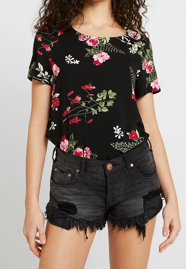 Top negro con estampado floral en rojo y verde, combinado con pantalones cortos de mezclilla negra desgastada que presentan dobladillos deshilachados y acentos metálicos.