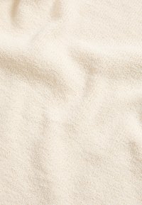 Tissu tricoté couleur crème avec un motif doux et texturé et des plis subtils créant des ombres délicates.