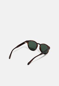 Tortoiseshell sunglasses with dark green lenses, round shape, and thin arms featuring a slight curve. Lightweight plastic material.
