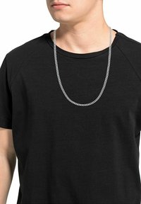 Collana in argento con catena metallica appoggiata su una t-shirt nera a girocollo, caratterizzata da una texture liscia e un design semplice, senza ulteriori dettagli.
