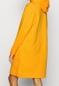 Oranges Kapuzenkleid aus weichem Stoff, mit lockerer Passform, langen Ärmeln und einer geräumigen Kapuze. Verfügt über gerippte Bündchen und Saum.
