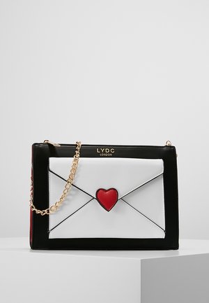 Bolso rectangular en blanco y negro con detalle de corazón rojo, asa de cadena dorada y la marca LYDC London en el centro superior.