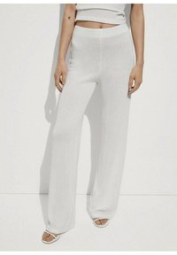 Pantaloni bianchi a gamba larga realizzati in materiale testurizzato, con vita alta e un fit morbido, abbinati a semplici sandali bianchi.