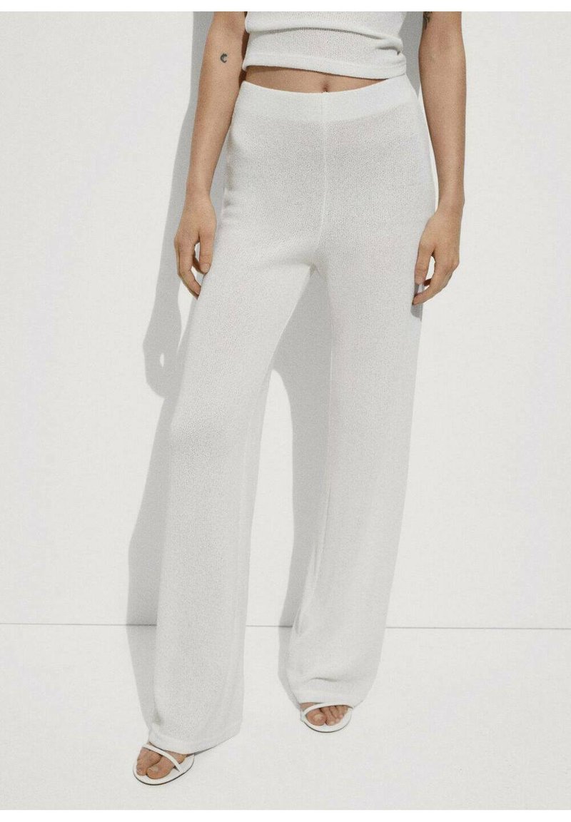 Pantaloni bianchi a gamba larga realizzati in materiale testurizzato, con vita alta e un fit morbido, abbinati a semplici sandali bianchi.