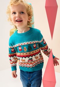 Tyrkysový pletený sveter s vianočnými vzormi, zobrazujúci Santa Clausa, stromy a soby, v kombinácii s modrým denimom. Geometrické ružové prvky na pozadí.